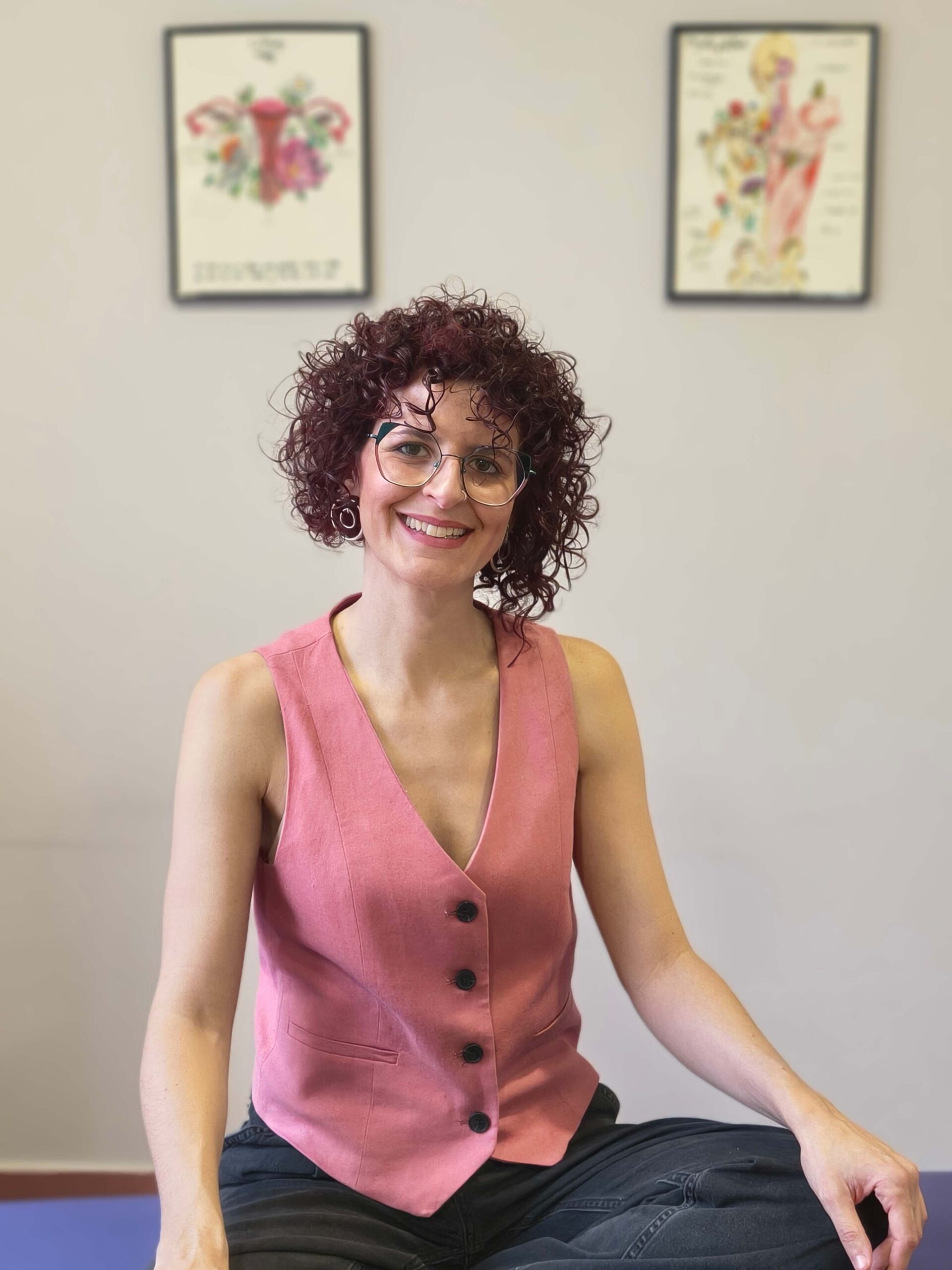 Especialista sentada junto a una camilla sostiene un modelo anatómico mientras sonríe.